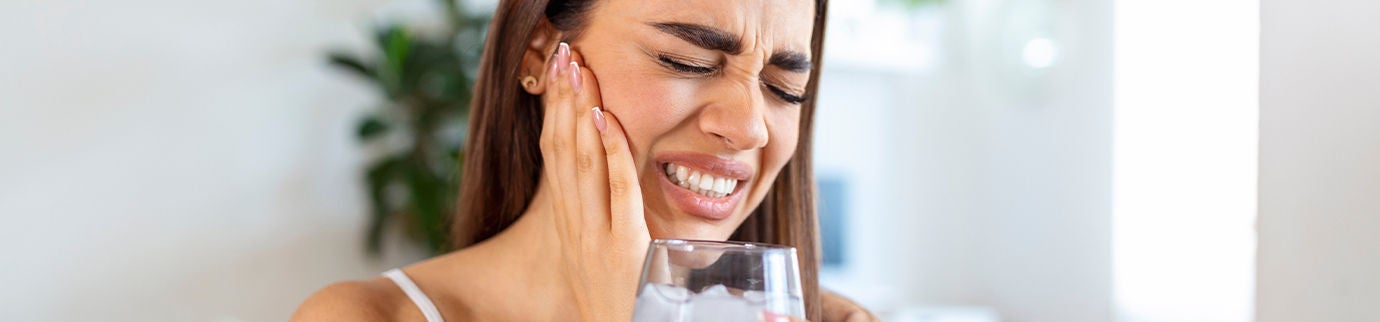 Mulher sentada segurando um copo d’água gelada, sugerindo sensibilidade nos dentes por problemas gástricos recorrentes.