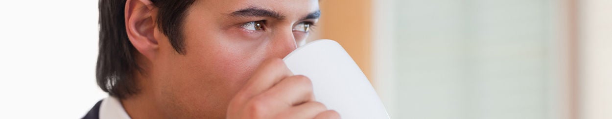 Homem tomando café em uma caneca branca no escritório, pensando se pode tomar café após implante dentário.