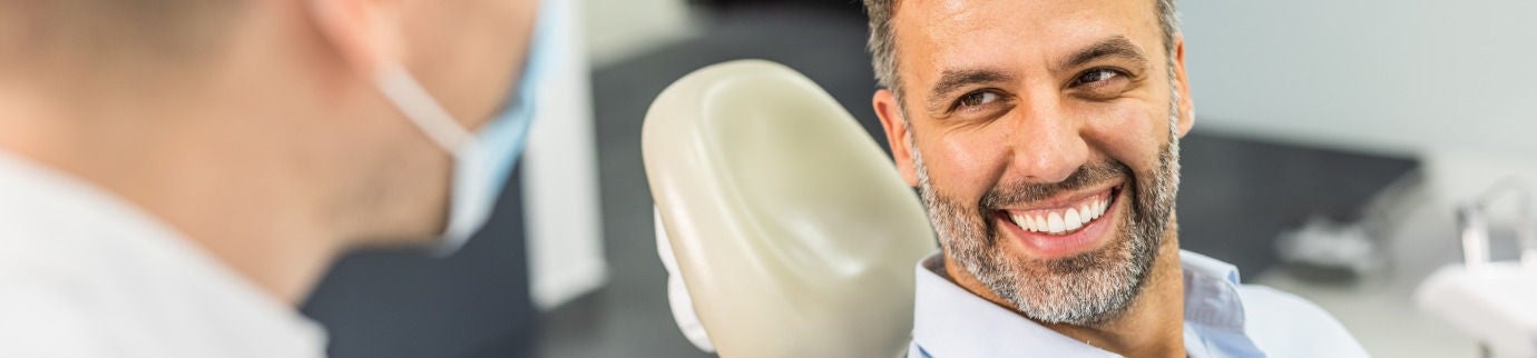 Homem no consultório do dentista recebendo dicas de como prevenir o envelhecimento dos dentes.