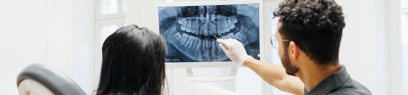 Dentista mostra radiografia para paciente, explicando possíveis danos na dentina durante a consulta odontológica.