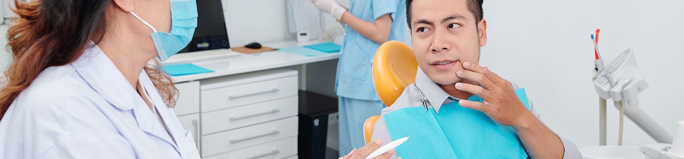 Dentista conversa com paciente no consultório, esclarecendo se quem tem implante dentário pode fazer ressonância.