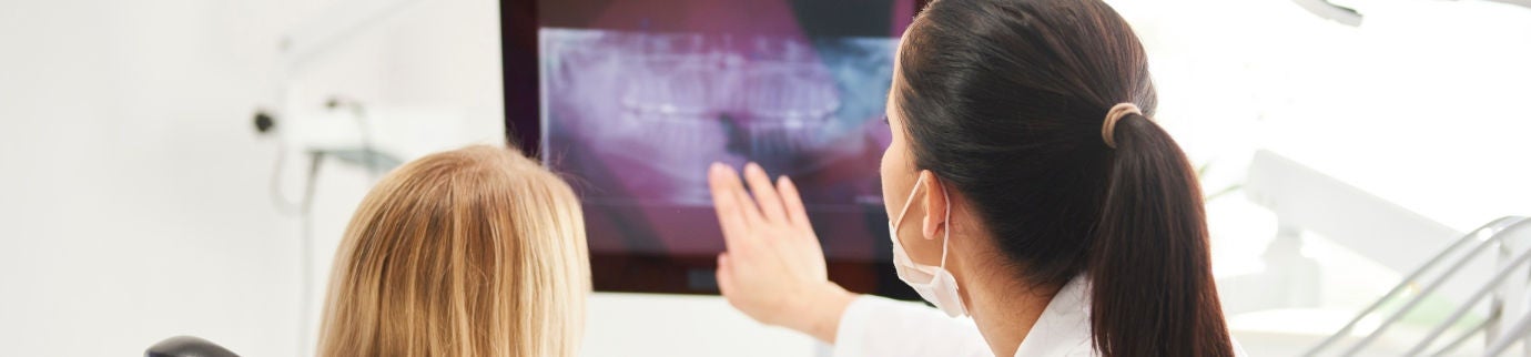 Dentista orienta paciente no consultório enquanto mostra radiografia, explicando cuidados após extração do siso.