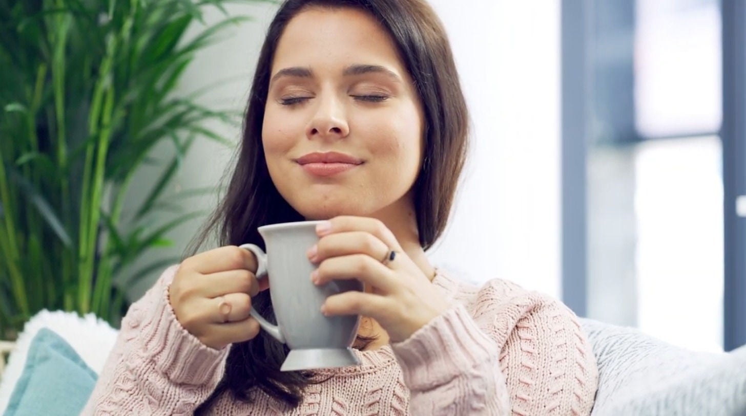 Mulher com um leve sorriso no rosto, segurando uma caneca em um momento de pausa, essencial para manter a concentração.