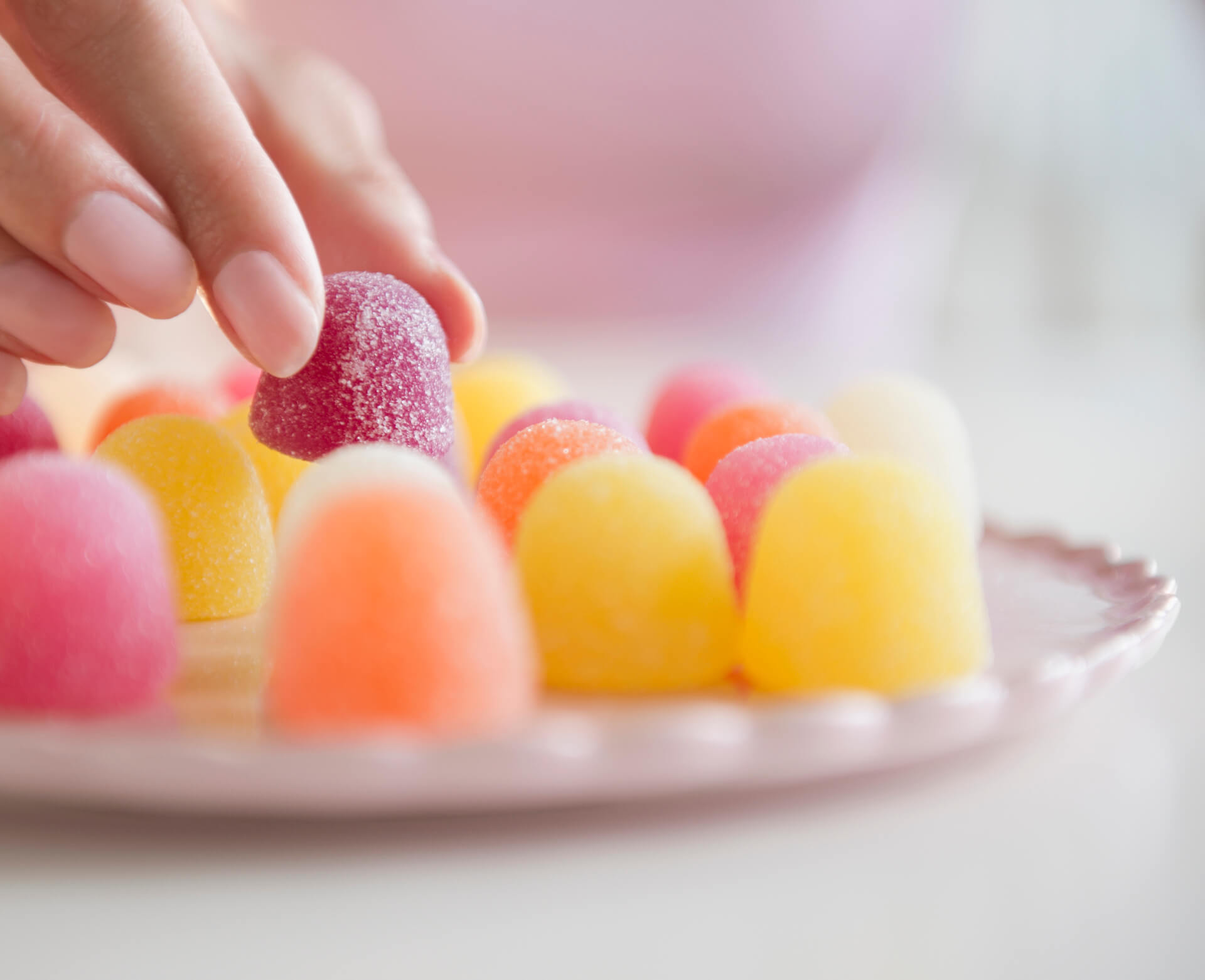 Uma mão delicadamente segurando uma bala de goma colorida, representando que a dor de dente ao comer doce não é causada pelo açúcar em si. Uma mão delicadamente segurando uma bala de goma colorida, representando que a dor de dente ao comer doce não é causada pelo açúcar em si.